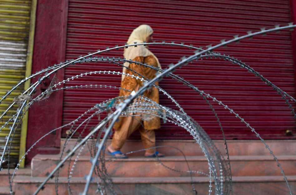 A Kashmiri woman walks past a barbed wire barricade set up by paramilitary soldiers during restrictions in Srinagar on Friday, September 27, 2019.