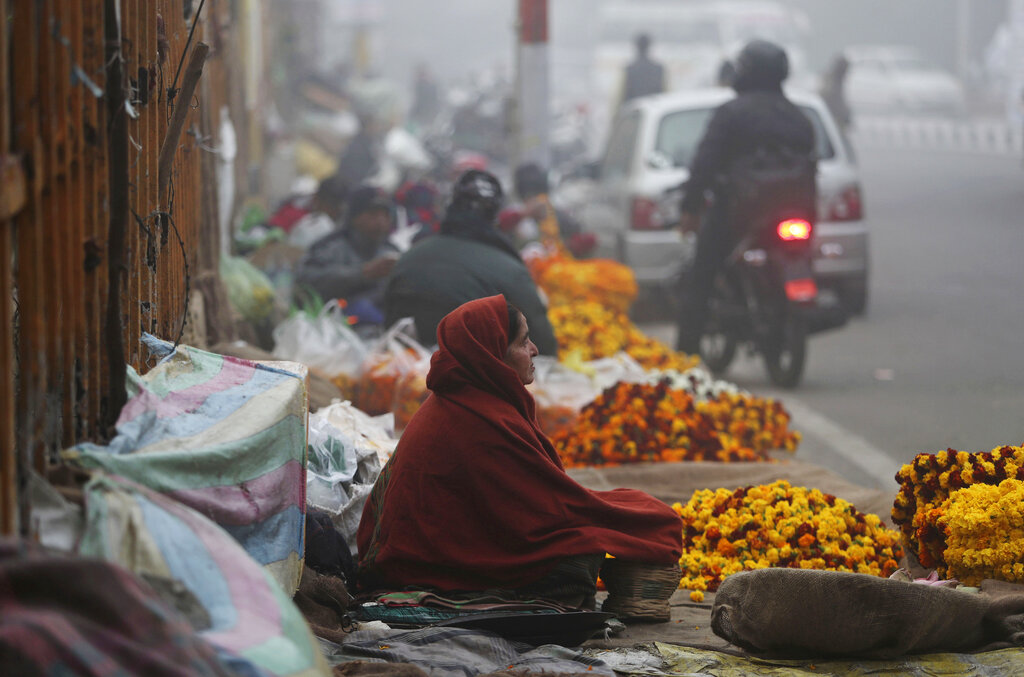 A flower vendor warms herself with a traditional Kashmiri fire pot on a cold and foggy morning in Jammu