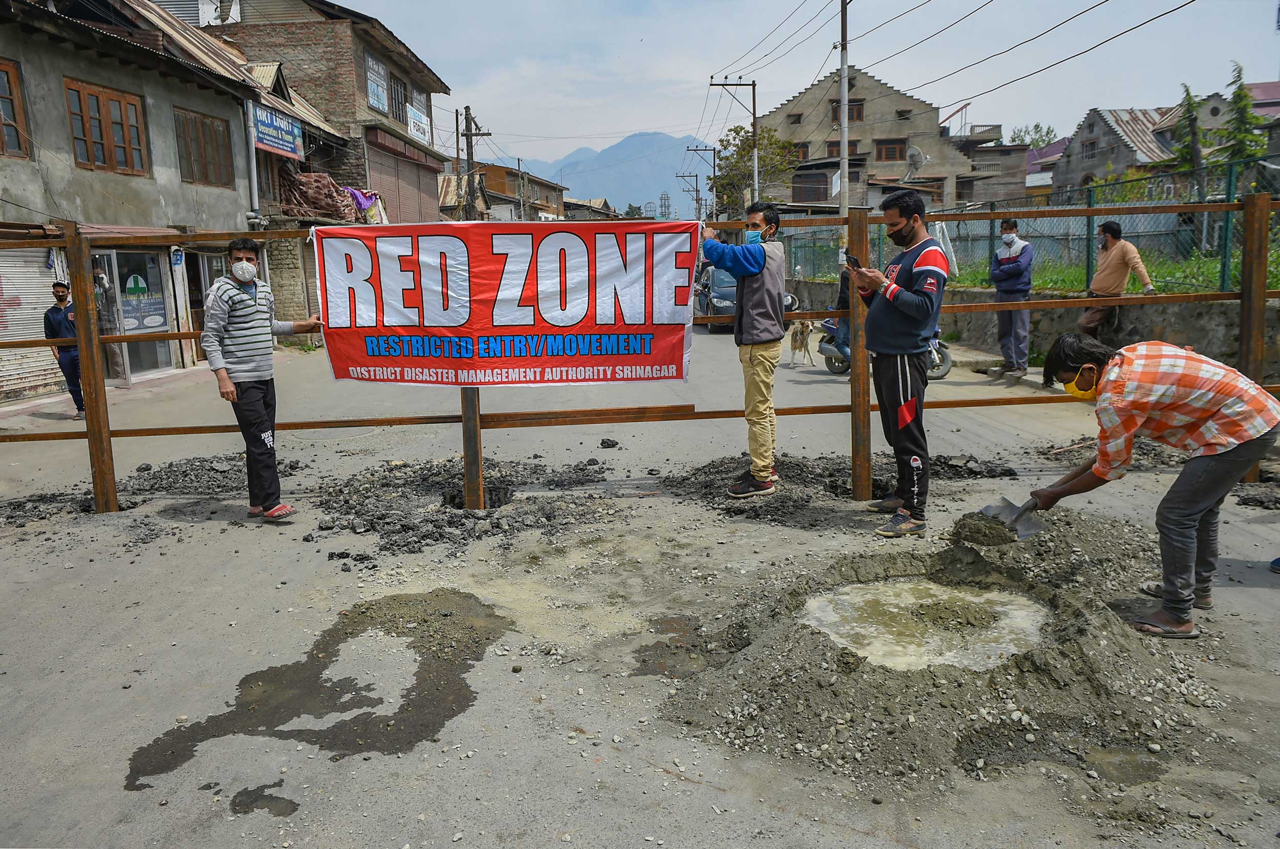 Workers place a banner after setting up a road blockade at a Covid-19 red zone area in Srinagar on Tuesday.