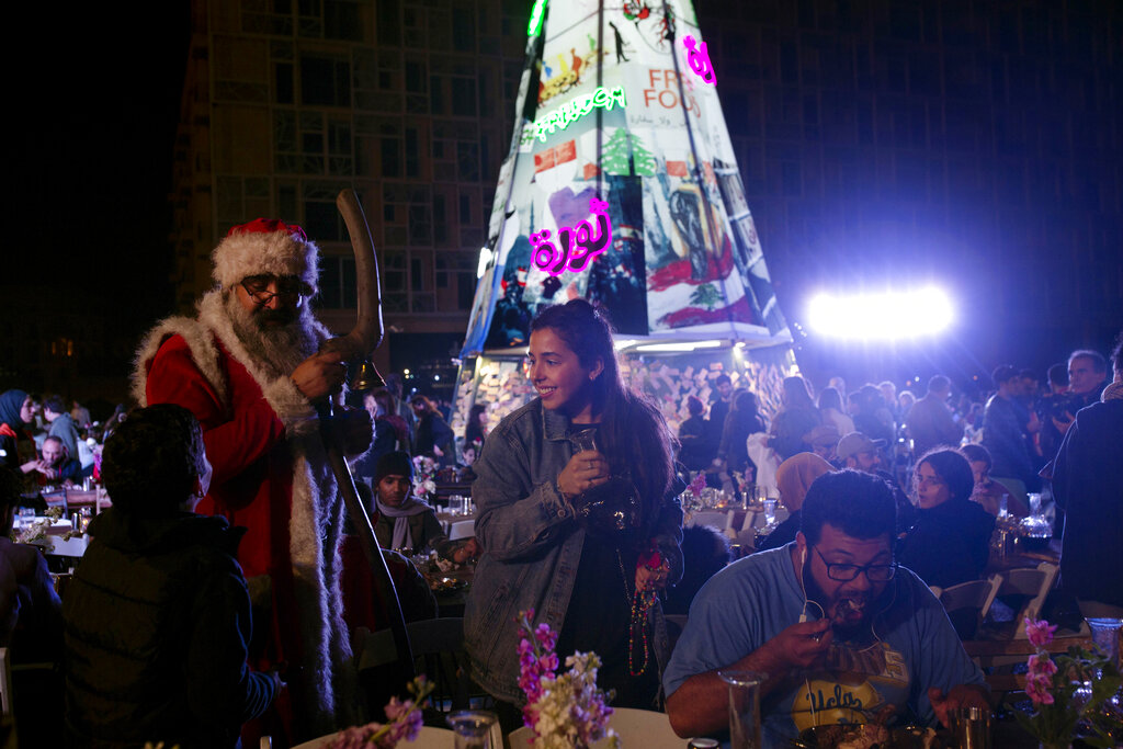 A volunteer, centre, serves drinks at a public Christmas dinner as a boy asks Santa Claus for a selfie, in Martyrs Square where anti-government activists are encamped, in Beirut, Lebanon. As Lebanon's protest movement enters its third month, the economic pinch is hurting everyone. But Lebanese are resorting to what they've done in previous wars and crises: They rely on each other, not the state.