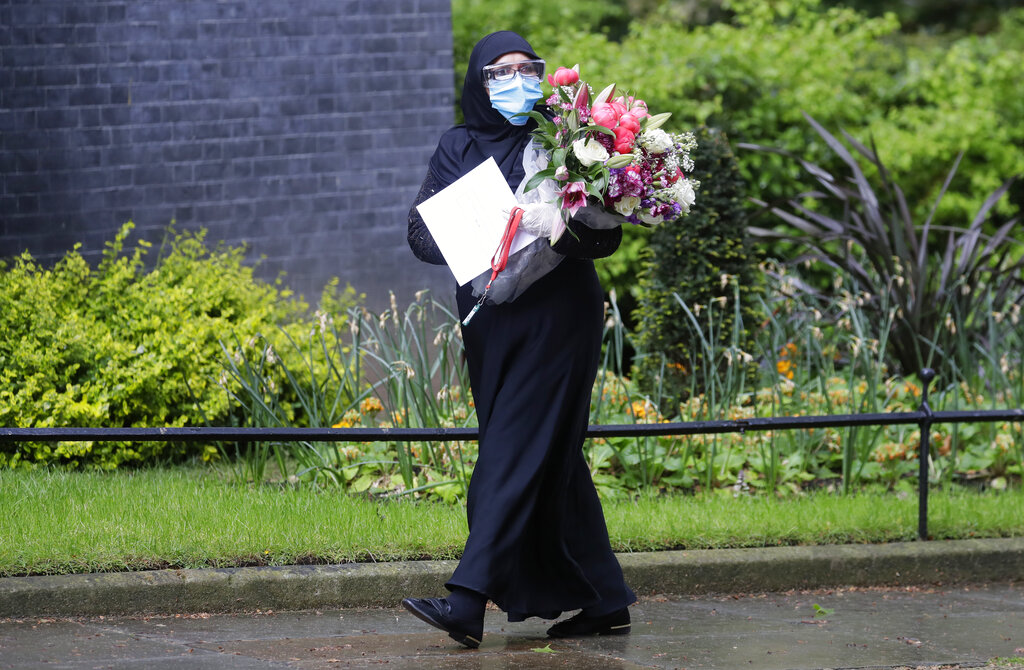 A woman wearing a mask and safety glasses to protect from coronavirus walks in Downing Street to deliver flowers from Imran Khan, the Prime Minister of Pakistan to 10 Downing Street in London, Thursday, April 30, 2020, after British Prime Minister Boris Johnson's partner Carrie Symonds gave birth.