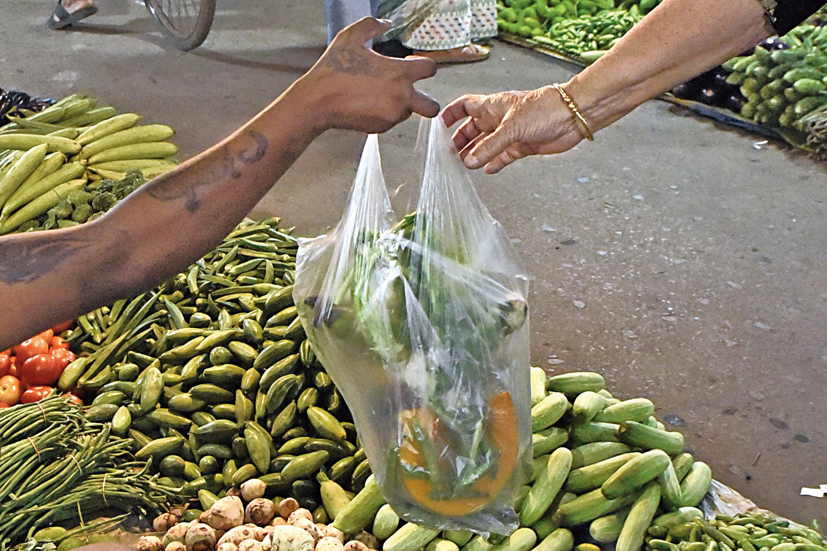 A vendor hands a customer vegetables in a thin plastic carrier bag at the Maniktala market on Tuesday. 

