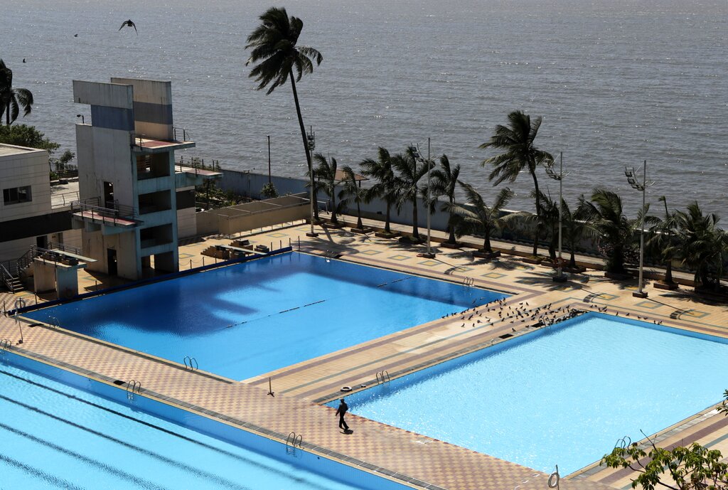 An attendant walks between the public swimming pools after closed by authorities as a precautionary measure against COVID-19 in Mumbai, India, Saturday, March 14, 2020. For most people, the new coronavirus causes only mild or moderate symptoms. For some, it can cause more severe illness, especially in older adults and people with existing health problems.