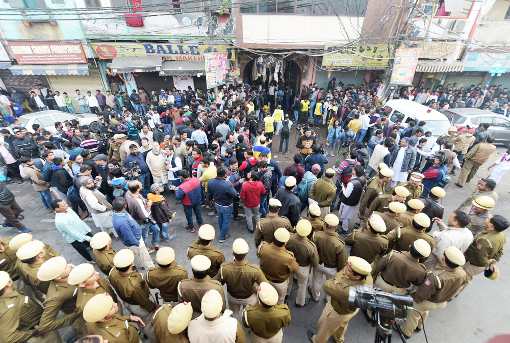 Police personnel and onlookers stand near a factory at Rani Jhansi Road where a major fire broke out, in New Delhi on Sunday morning, December 8, 2019. At least 43 labourers were killed and several others injured in the mishap.