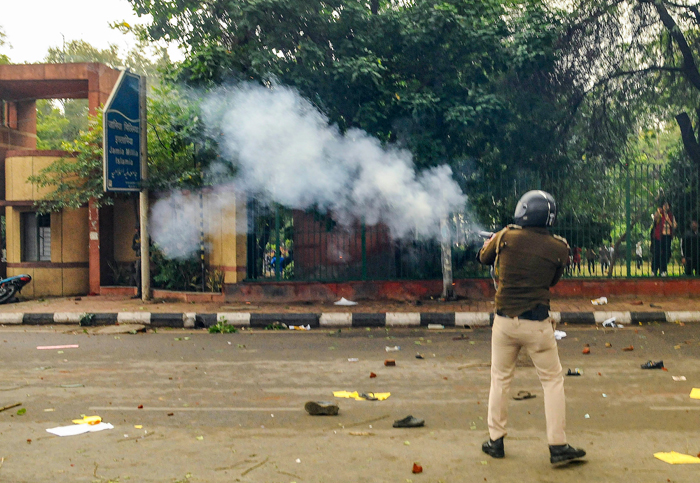 A policeman fires tear gas as students of Jamia Millia Islamia University stage a protest against the passing of Citizenship Amendment Bill, in New Delhi
