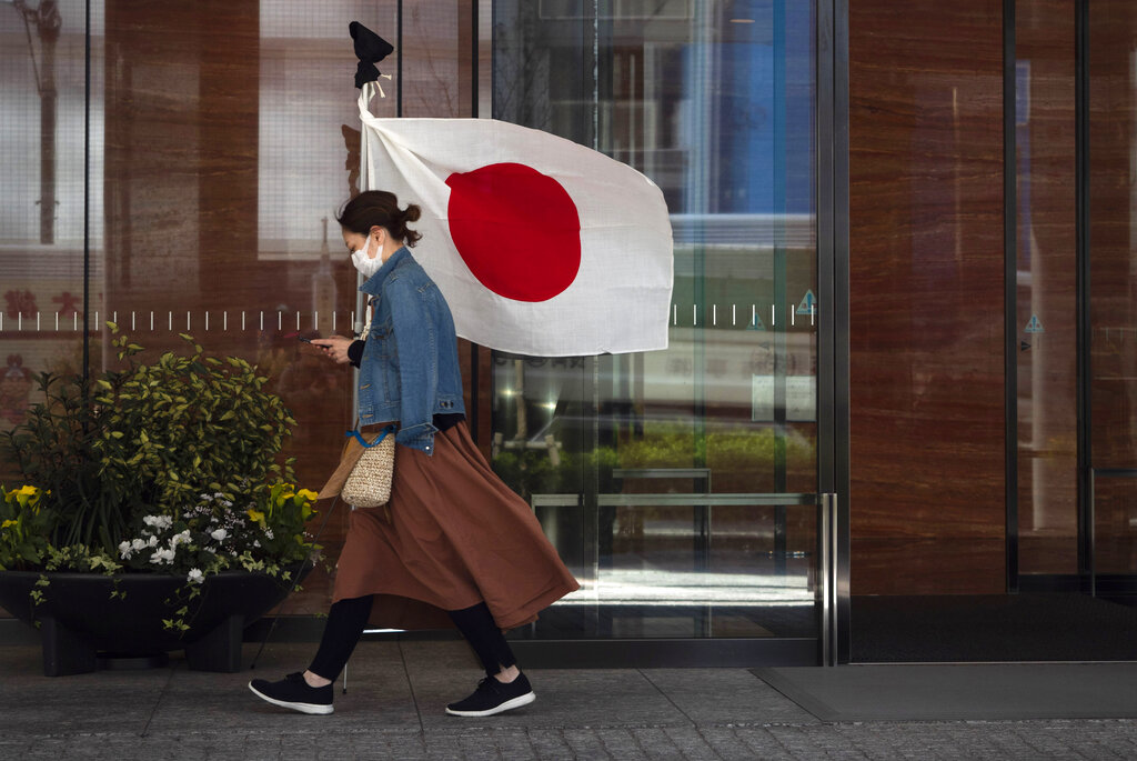 A woman wearing a mask walks past a Japanese flag Wednesday, March 11, 2020, in Tokyo.