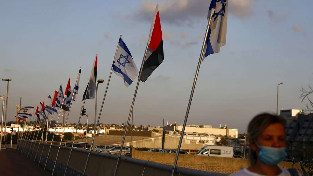A woman wearing a face mask against the coronavirus walks past United Arab Emirates and Israeli flags at the Peace Bridge in Netanya, Israel, Sunday, Aug. 16, 2020. 