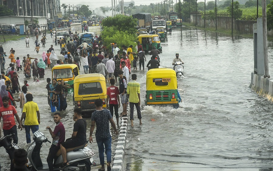 Commuters wade through a waterlogged street during heavy rains, in Surat on Friday.