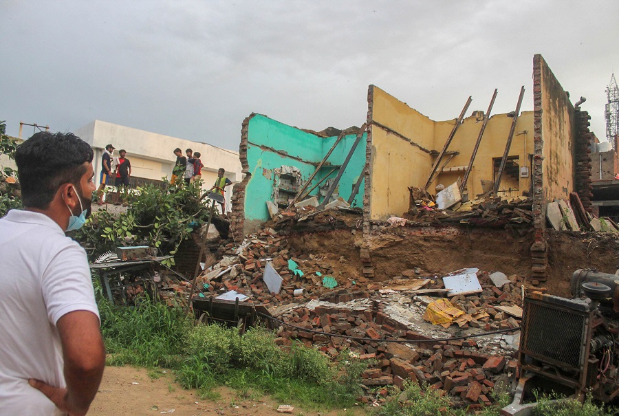 A passerby looks at a partially collapsed structure after a banyan tree fell on it during heavy rain, in Gurugram on Thursday.