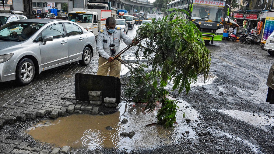 A policeman places a tree branch in a pit on a damaged road to prevent any mishap, following heavy rains, in Thane on Tuesday.