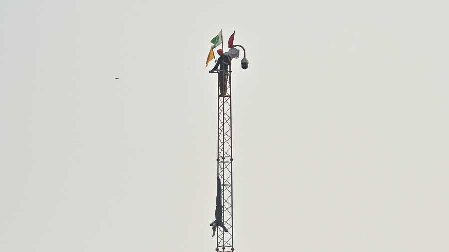 A farmer climbs up a tower to fix his organisation’s flag during the ongoing protest against the new farm laws at the Singhu border between  Delhi and Haryana on Sunday. 