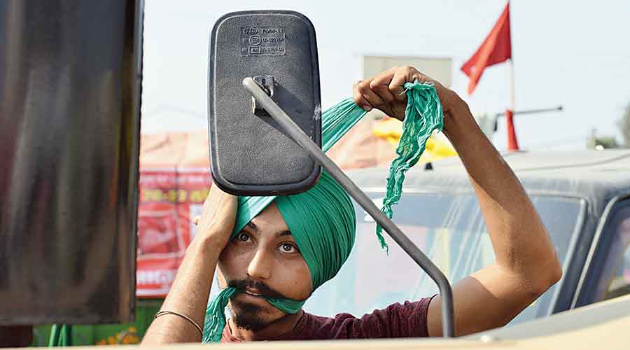 A farmer at the protest looks in the mirror as he ties his turban