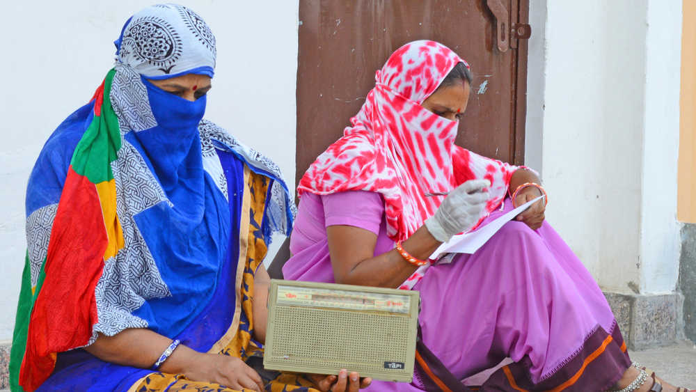 Anganwadi workers listen to the radio during a door-to-door survey to check the spread of coronavirus.