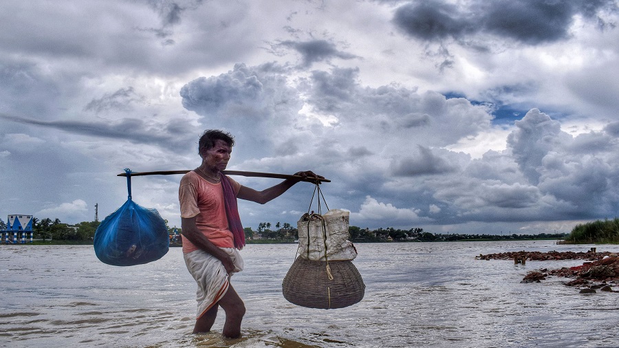 A man carrying his belongings walks at the banks of Hooghly river in the backdrop of dark clouds looming in the sky, in Nadia district