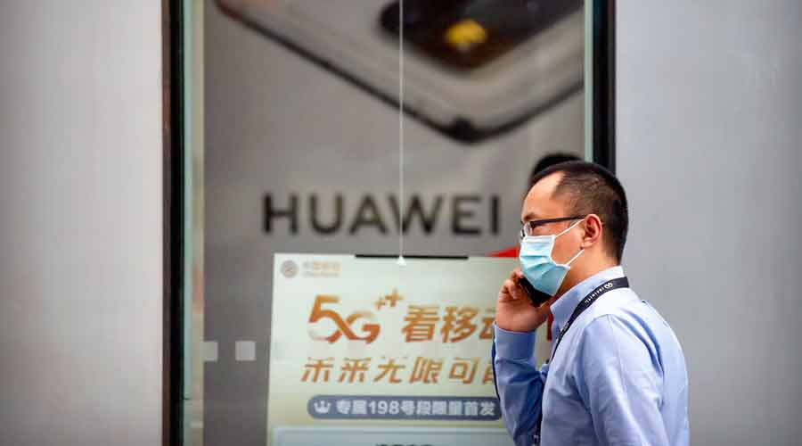 A man wearing a face mask to protect against the new coronavirus talks on his smartphone as he walks past a Huawei store in Beijing, Wednesday, July 1, 2020. 