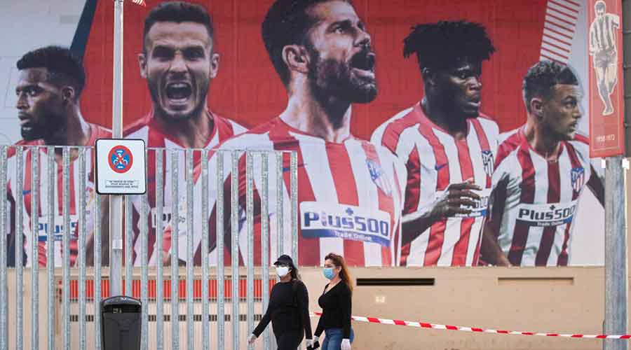 In this May 5, 2020 file photo, two women wearing face masks pass by a giant poster of Atletico Madrid soccer players at the Wanda Metropolitano stadium in Madrid, Spain.