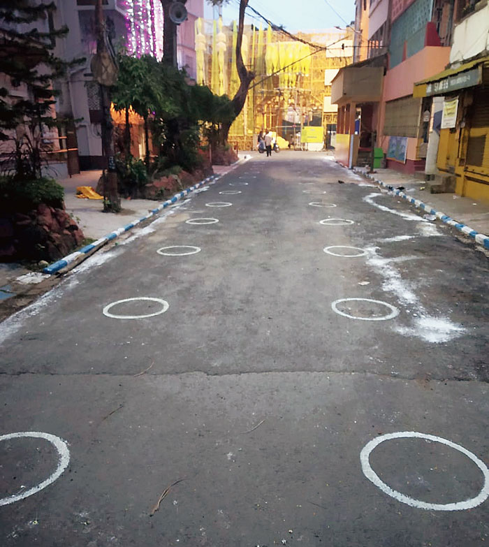 White circles drawn on a road leading to Mudiali Club that will help pandal-hoppers maintain safe distance from each other