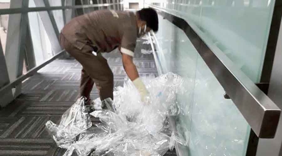 An airport employee removes face shields and PPE packets discarded  by passengers on an aerobridge