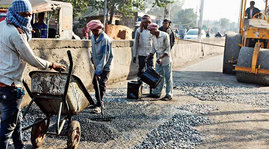 Workers carry out a repair work on Bank Mor-Jharia Road on Monday.