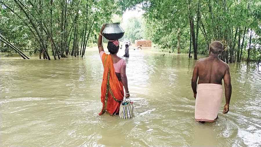 A woman carries drinking water in bottles and an aluminium pot in the  flood-hit  Khanakul on Thursday.