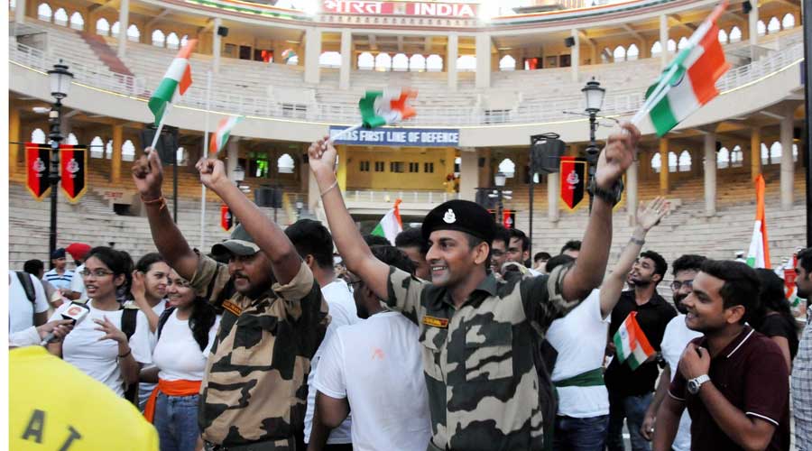 Visitors wave the national flags during a ceremony on the occasion of 75th Independence Day, at the Attari-Wagha border