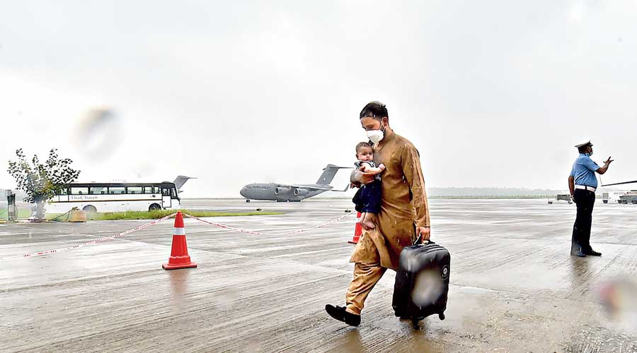 A man carries a child as people stranded in Afghanistan arrive by an Indian Air Force repatriation flight at the Hindon Air Force Station in Ghaziabad on Sunday