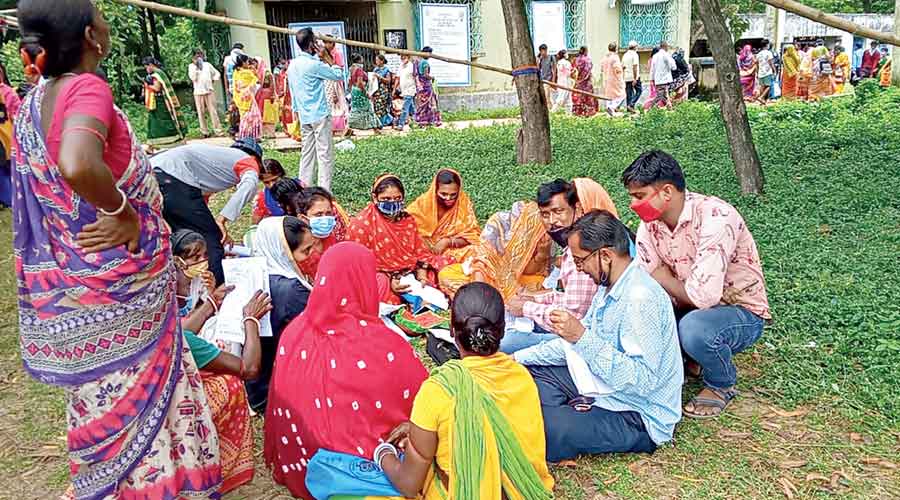 CPM supporters help women fill up forms for Lakshmir Bhandar at Kanksa in East Burdwan. 