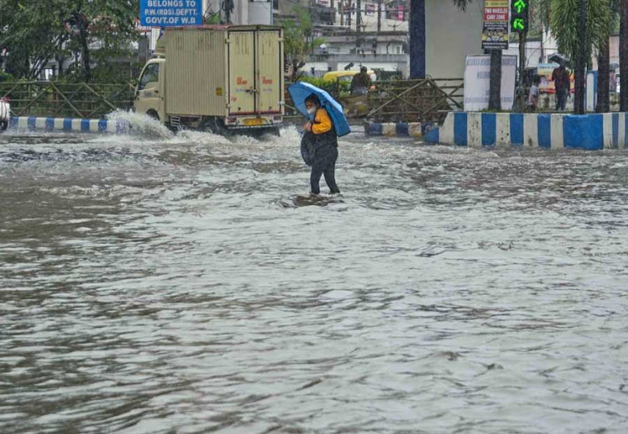A young woman struggles to balance her umbrella and her backpack while wading through a waterlogged street near Haldiram's crossing on VIP road