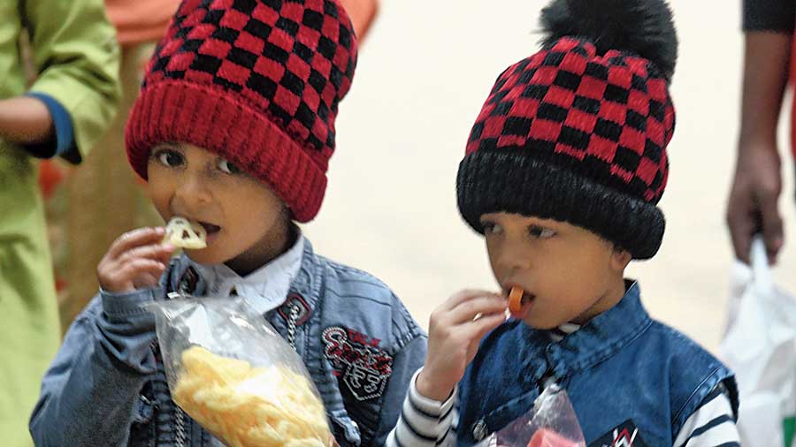 Two children, dressed in woollens, enjoy savouries at Prinsep Ghat on Monday evening.