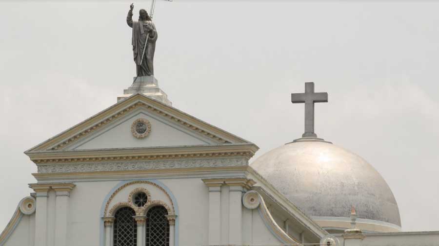 A statue of Jesus holding a cross on the front pediment, with the great dome of the church in the background