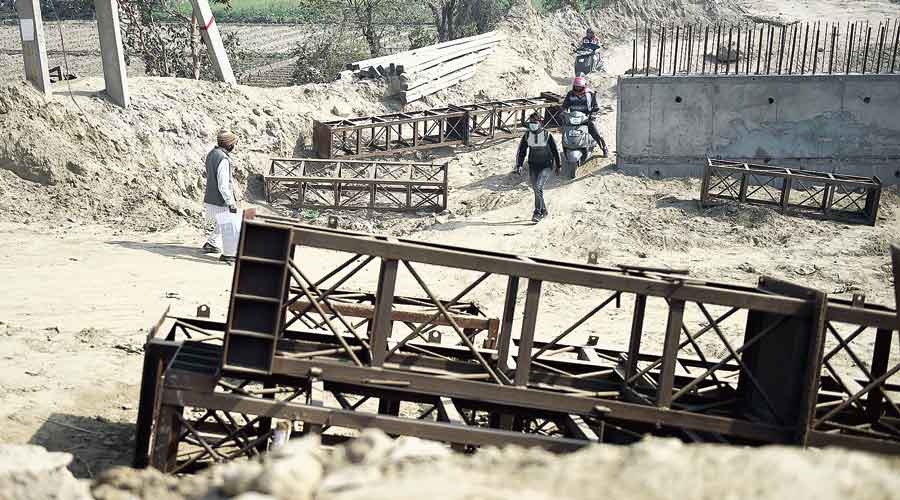 Commuters pass through an unmetalled path on Tuesday to cross the Singhu border where road blockades have been put up by security personnel