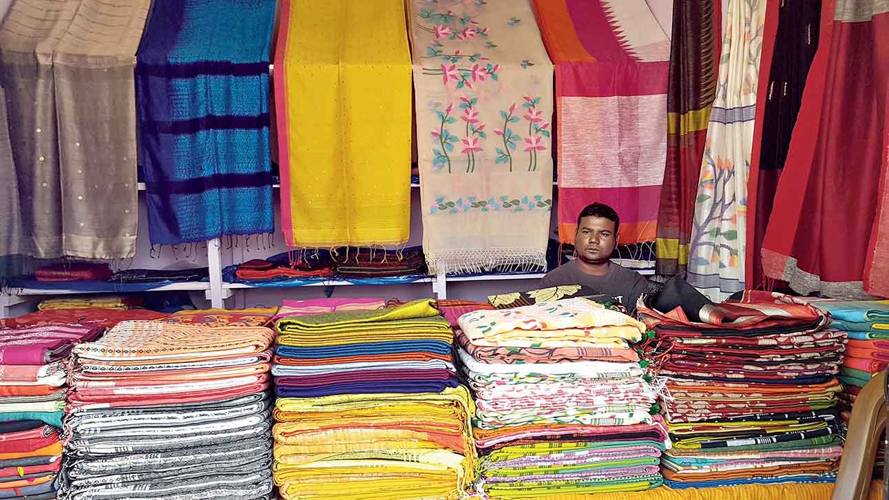 A stall keeper at Banglar Tanter Haat with stacks of saris to sell. 