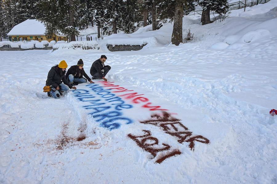 Tourists sit near Happy New Year 2021 sign on snow at the famous ski resort of Gulmarg in north Kashmir on the eve of the New Year on Thursday.