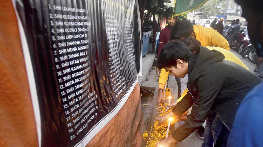 Protesters light candles in front of a banner listing the names of people who have died at  the farmers’ siege at the doors of Delhi