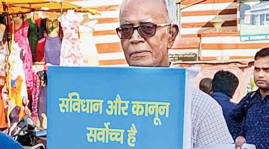 File picture of Stan Swamy holding a banner that says the Constitution and law are above all. 