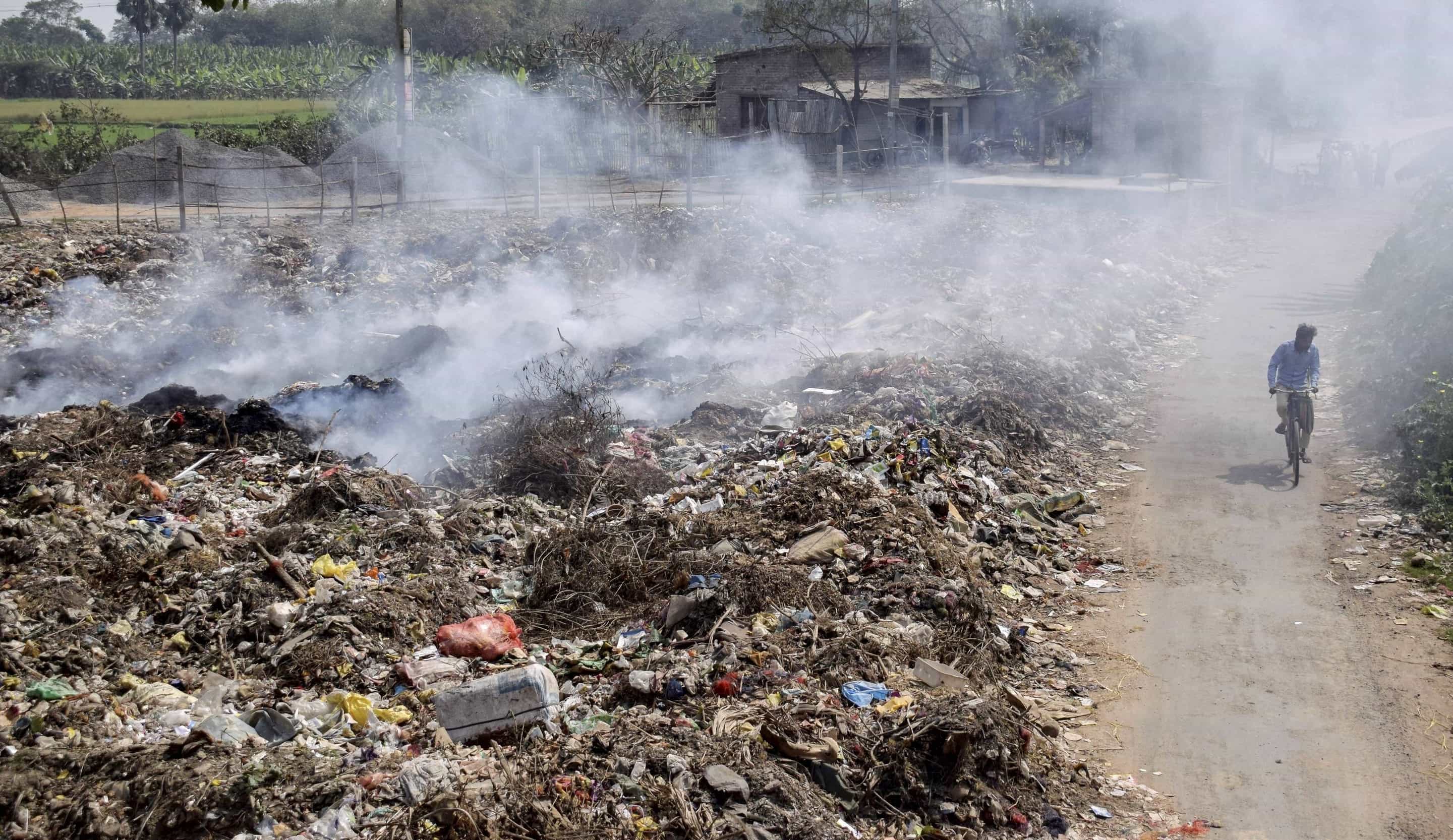 A man on a cycle passes through a dumping ground in Nadia as smoke billows from the garbage on Saturday.