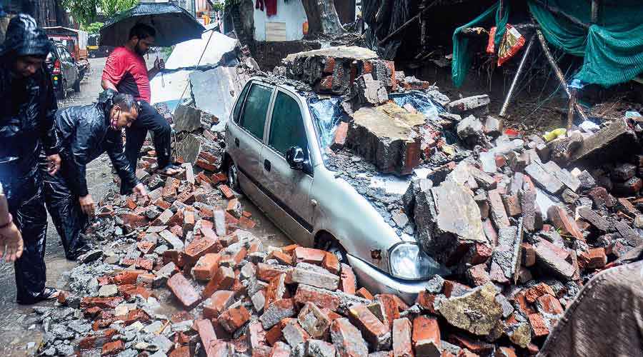 A car is damaged after a society compound wall fell on it at Savarkar Nagar in Thane on Wednesday.