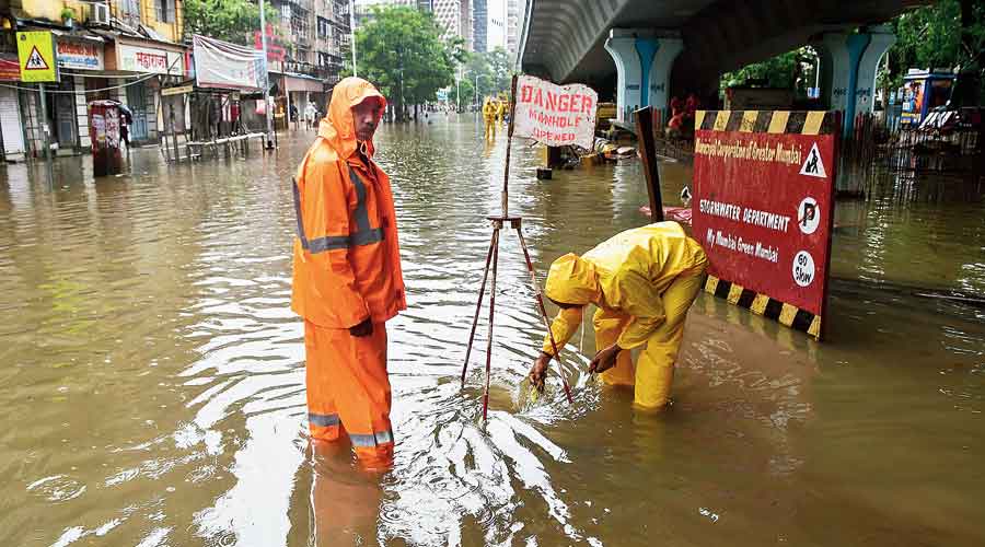 BMC workers install a signboard near a manhole to guide people on a waterlogged road at Parel on Wednesday