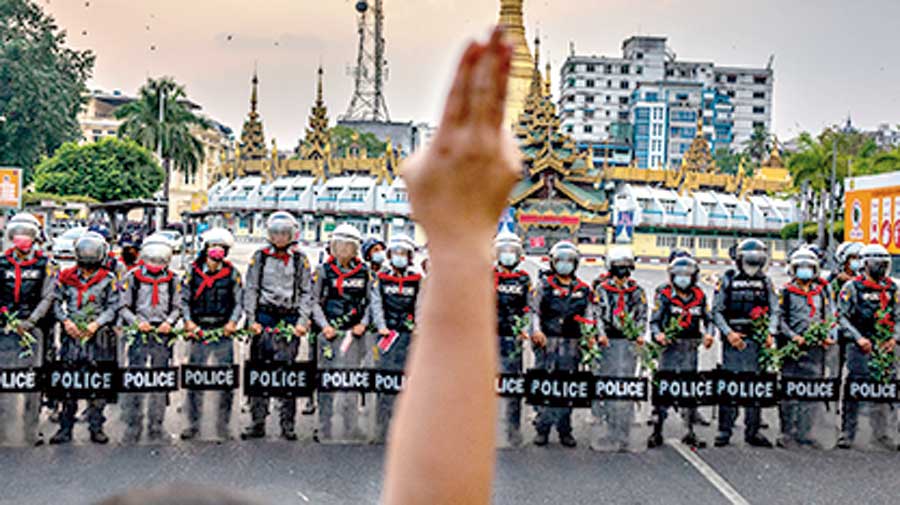 A protester makes a three-finger salute in front of a row of riot police, who are holding roses given to them by protesters, on February 06, 2021 in Yangon, Myanmar. 