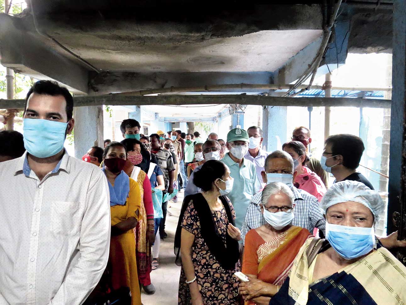 then and now: Senior citizens stand in queue next to the queue of polling personnel and police at Bidhannagar Subdivisional Hospital last Friday. Picture by Sudeshna Banerjee. (Below) The current seating arrangement in air-conditioned space on the second floor for senior citizens