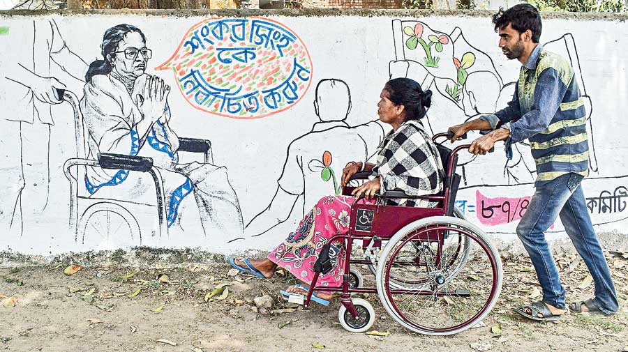 A woman being wheeled away in front of a wall graffiti of Mamata Banerjee seeking votes riding a wheelchair in Nadia\xe2\x80\x99s Santipur