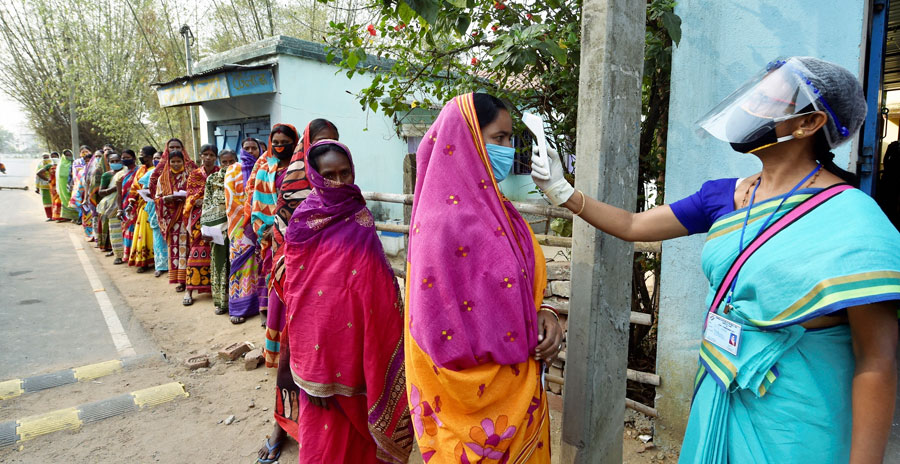 Voters undergo thermal scanning, as precaution against Covid-19, while waiting to cast votess at a polling station, during the first phase of West Bengal Assembly elections, at Sirshi in Jhargram, Saturday