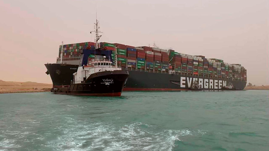 A boat navigates in front of the Ever Given, a container ship operated by a company called Evergreen. 