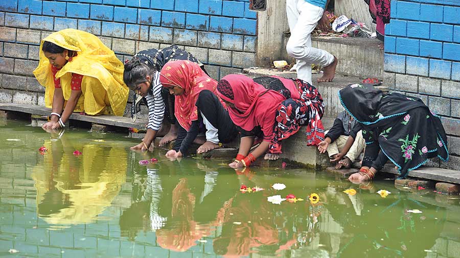 A Hindu woman (in yellow sari) prays at the pond in the Ghutiari Sharif compound with Muslim women