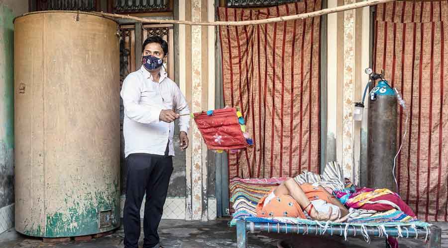 Dinesh Kumar, 32, fans his mother Chandravati Devi, 55, as she rests in a cot while receiving oxygen support at her home in Mewla Gopalgarh