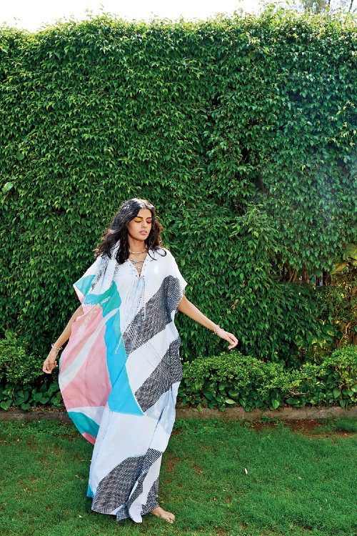 A flowy handbrush-painted kaftan comes with an abstract eyelet detailing in the shades of sea green, sea blue, peach and black and sports a modern criss-cross drawstring neckline to complement the bold print.