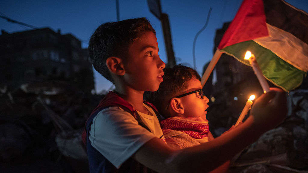  Palestinian children hold candles during a rally amid the ruins of houses destroyed by Israeli strikes, in Beit Lahia Northern Gaza Strip on May 25, 2021 in Gaza City, Gaza. 