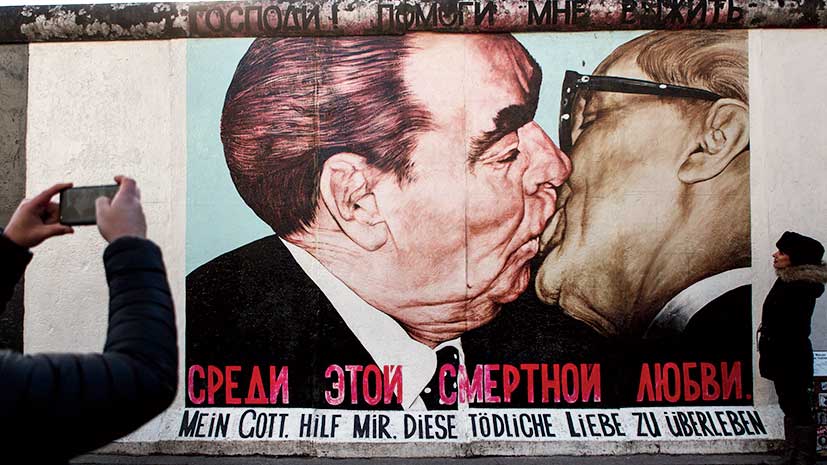 Visitors stand in front of a mural depicting former Soviet leader Leonid Brezhnev kissing former communist East German leader Erich Honecker at the East Side Gallery, which is a surviving remnant of the Berlin Wall, on February 5, 2018 in Berlin, Germany. Today has been 10,316 days since the Berlin Wall officially fell, the same number of days that it stood between 1961 and 1989. The Berlin Wall, built by the communist authorities of East Germany, divided capitalist West Berlin from communist East Berlin and came to symbolize the Cold War between the western Allies, led by the United States, and the Eastern Bloc, led by the Soviet Union. 