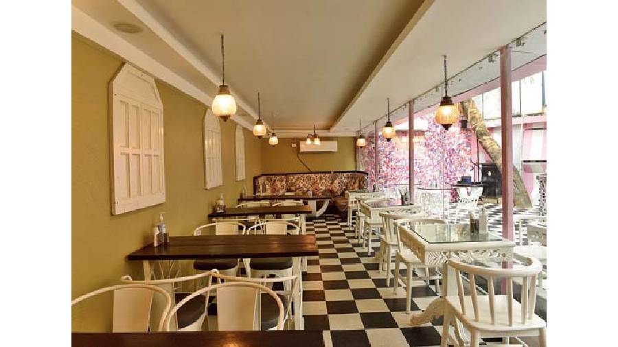 The lounge is a 35-seater area. The white glass and wooden tables complement the floral printed seating arrangement and bright yellow hanging lights.