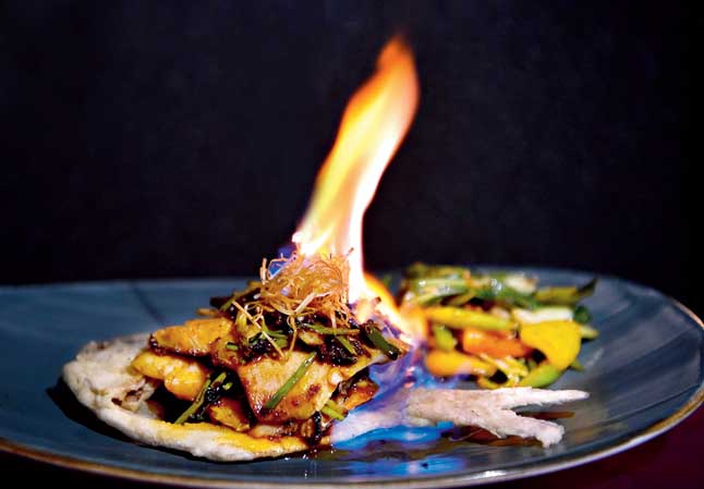 Whole Pomfret Ikan Bakar is drama on a plate. The Indonesian-style grilled pomfret is served with spicy peanut sauce. The fish is lit and then the sauce is poured on top.